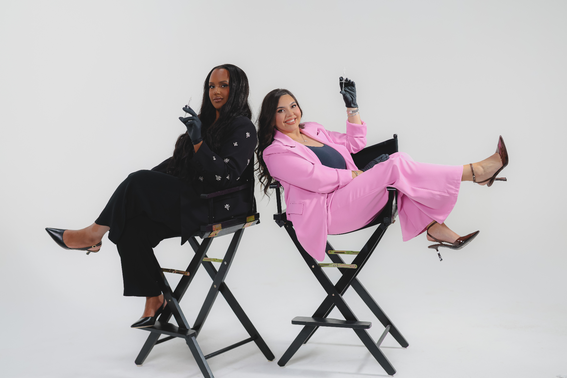 Nayah and Evelyn seated on director's chairs holding syringes